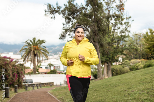Plus size woman jogging outdoor at city park - Main focus on headphones