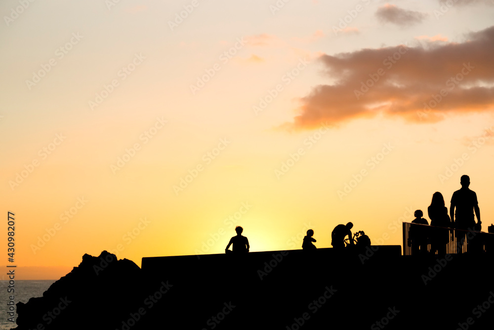silhouettes of caucasian man practicing yoga at sunset in sea promenade with people walking , Madeira island