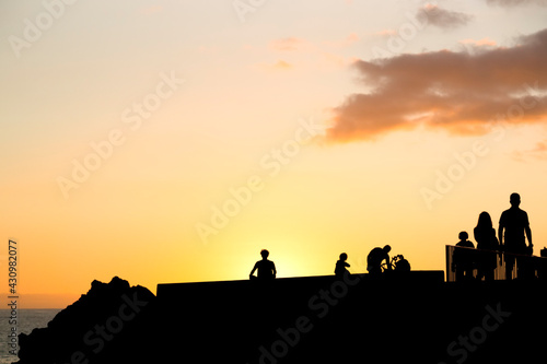silhouettes of caucasian man practicing yoga at sunset in sea promenade with people walking   Madeira island