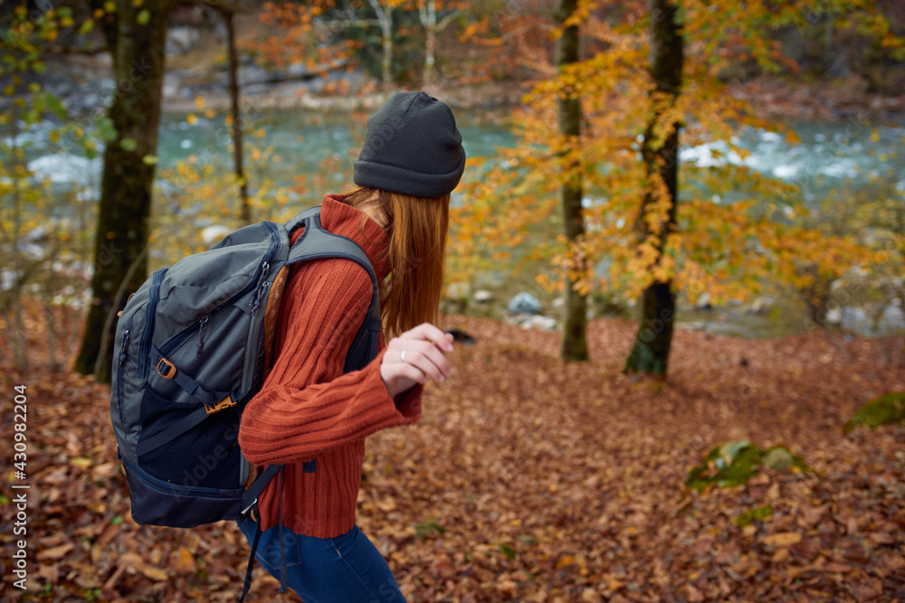 woman in a sweater with a backpack on her back near the river in the mountains and park trees autumn landscape woman in a sweater with a backpack on her back near the river in the mountains and park trees autumn landscape