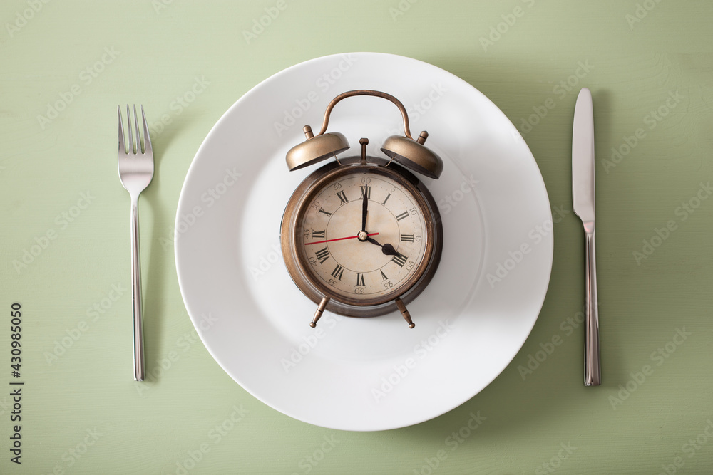 concept of intermittent fasting, ketogenic diet, weight loss. fork and knife, alarmclock on plate concept of intermittent fasting, ketogenic diet, weight loss. fork and knife, alarmclock on plate