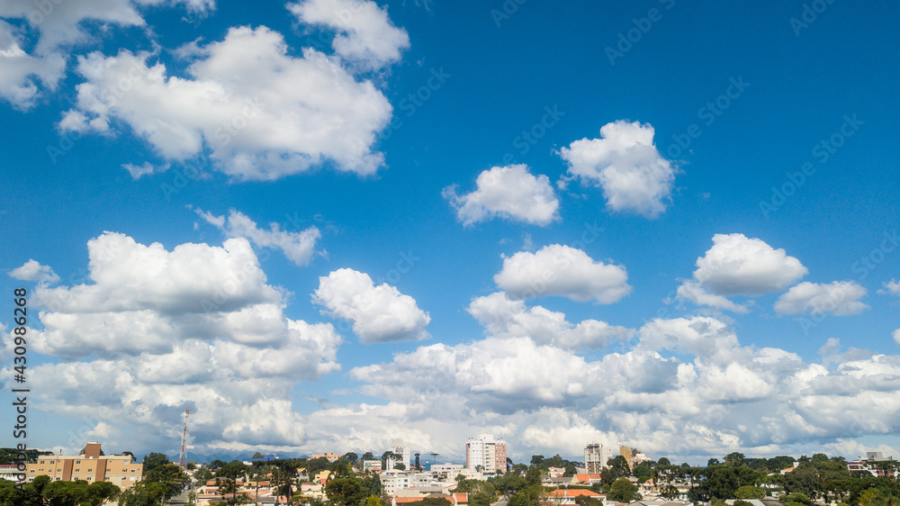Image of a day with the blue sky and some white clouds. At the base of the image is a city.
