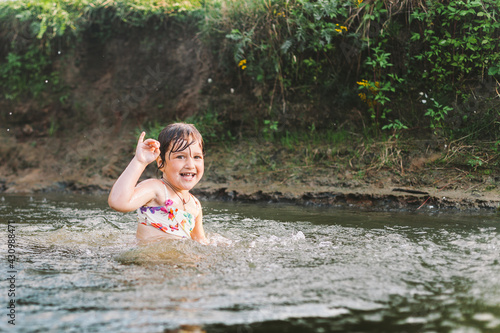 Happy summertime, healthy childhood concept. Little girl swimming, splashing, jumping and having fun in a river in summer. Blured green background. Horizontal shot.