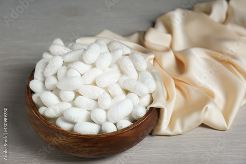 Cocoons with bowl and silk fabric on white wooden table