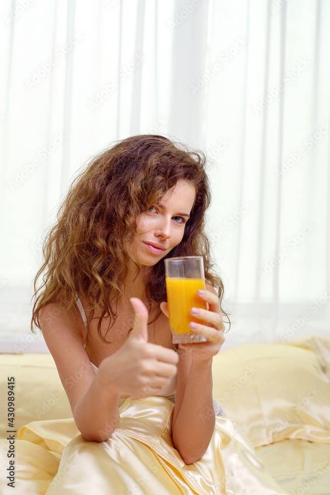 Cheerful woman drinking an orange juice sitting on her bed at home Cheerful woman drinking an orange juice sitting on her bed at home
