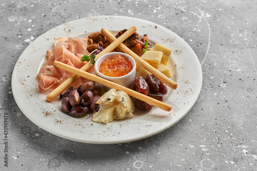 Set of snacks for wine. Prosciutto, parmesan, gorgonzola, almonds, olives, bread chips, mostard fruit confiture on gray marble background photo