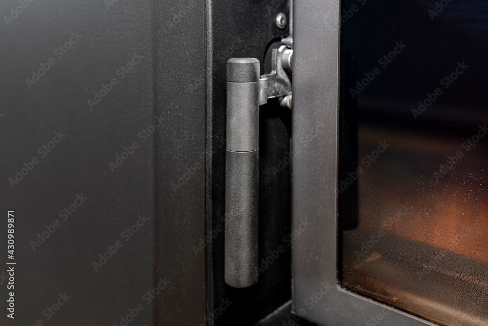 A handle and a closure in one in a modern fireplace with a closed combustion chamber standing in the living room in black. A handle and a closure in one in a modern fireplace with a closed combustion chamber standing in the living room in black.
