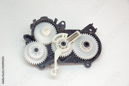 cogwheels mechanism in black plastic case. Part of inkjet printer: complex mechanical drive made of Multiple reducer gears of white plastic and spring