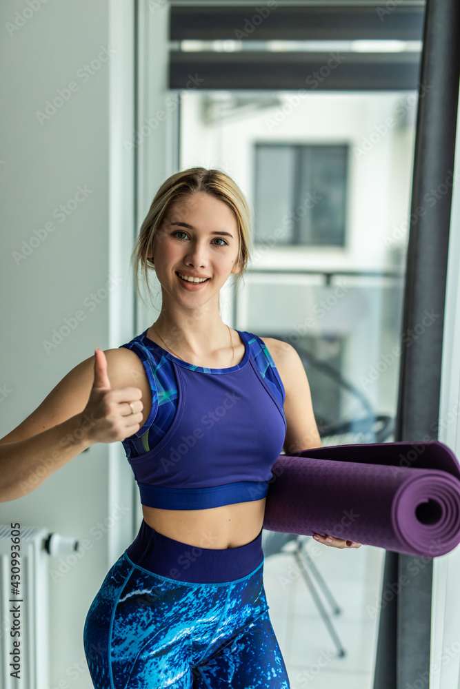 Portrait of smiling sporty woman, yoga, pilates or other fitness instructor, looking at camera, attractive successful female coach wearing sportswear, grey bra, holding yoga mat