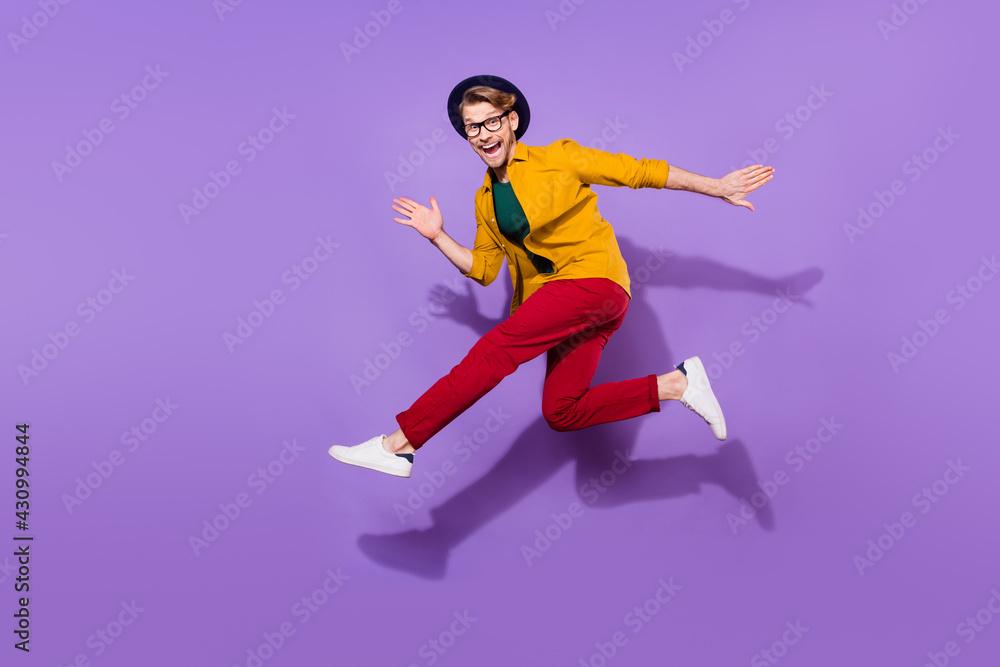 Full body profile side photo of young man happy positive smile jump go run fast hurry isolated over purple color background Full body profile side photo of young man happy positive smile jump go run fast hurry isolated over purple color background