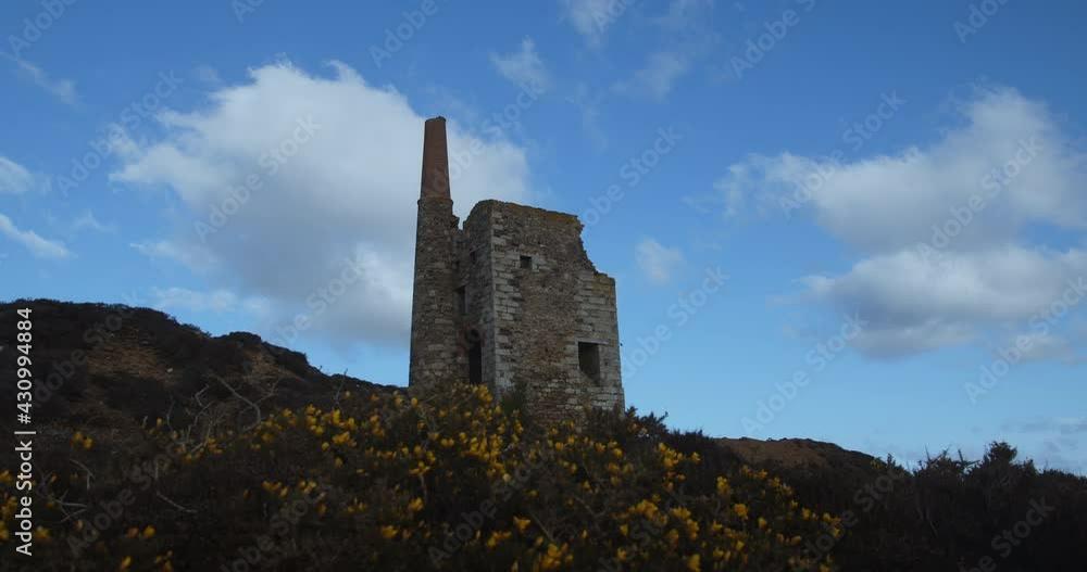 Ruin Of Cornish Tin Mine On Top Of A Valley With Yellow Flowers On Slope. Cornwall and West Devon Mining Landscape In England. low angle, slider shot Ruin Of Cornish Tin Mine On Top Of A Valley With Yellow Flowers On Slope. Cornwall and West Devon Mining Landscape In England. low angle, slider shot