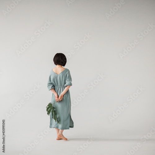 Fotografia Brunette girl with short hair in a mint dress made of natural fabrics, stands with her back to the viewer