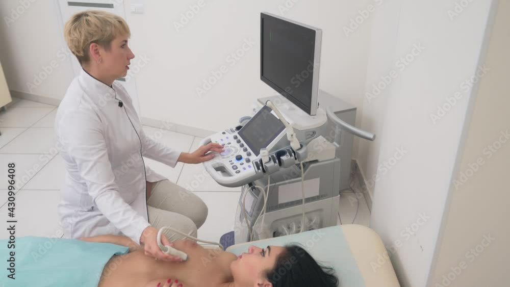 From above of middle aged mammologist using ultrasound device to examine naked breast of female patient. Young woman lying on coach in clinic office and covering nipple with hand. Concept of medicine. From above of middle aged mammologist using ultrasound device to examine naked breast of female patient. Young woman lying on coach in clinic office and covering nipple with hand. Concept of medicine.