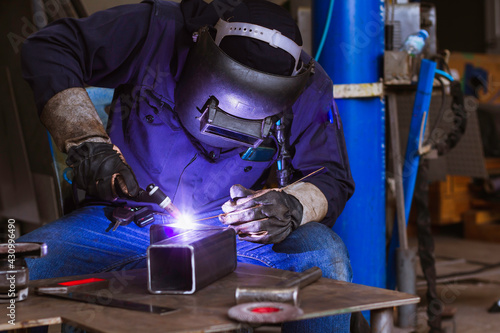 Welder is welding the steel in the factory. Weld the steel in dark. Workers wearing industrial uniforms and welding masks at a welding factory protect from welding sparks. Occupational safety concept