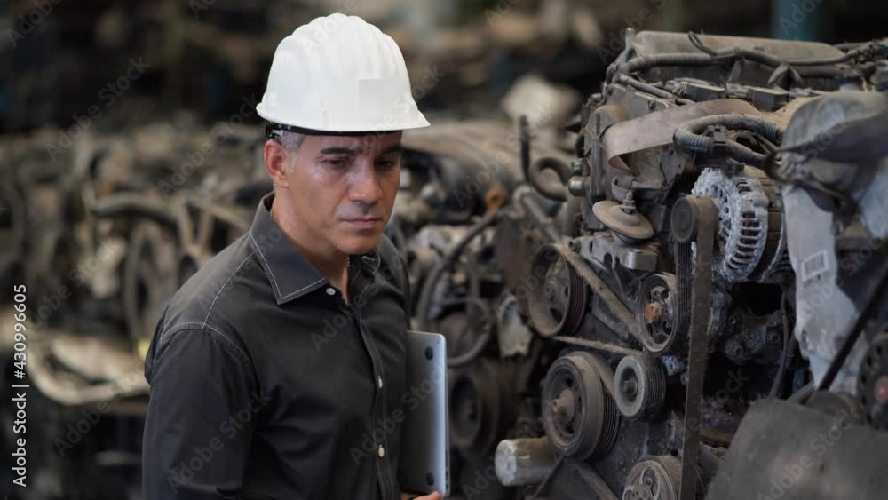 senior engineer using laptop computer checking list old used car engine in machinery parts shop warehouse. old technician man Repair vehicle automobile machine in Recycle motor factory senior engineer using laptop computer checking list old used car engine in machinery parts shop warehouse. old technician man Repair vehicle automobile machine in Recycle motor factory