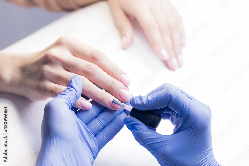Closeup manicure in spa salon. Woman applying base for gel pink nail polish with brush