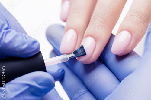 Manicurist uses brush to apply pink gel polish to woman client nail  concept process manicure