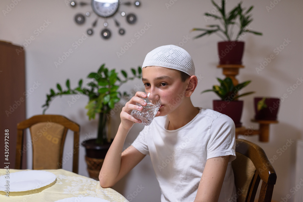 a boy in an Islamic costume drinks water during Iftar in the month of Ramadan. a boy in an Islamic costume drinks water during Iftar in the month of Ramadan.