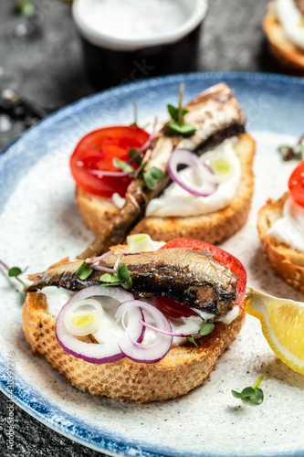 Sandwiches with sprats on toasted bread with fish, fresh tomatoes and onion. Food recipe background. Close up