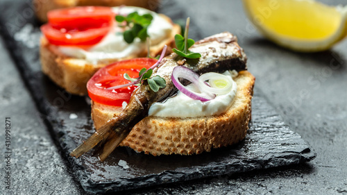 Sandwich with sprats, tomatoes, onion and microgreen on a slate board, Danish cuisine. Food recipe background. Close up