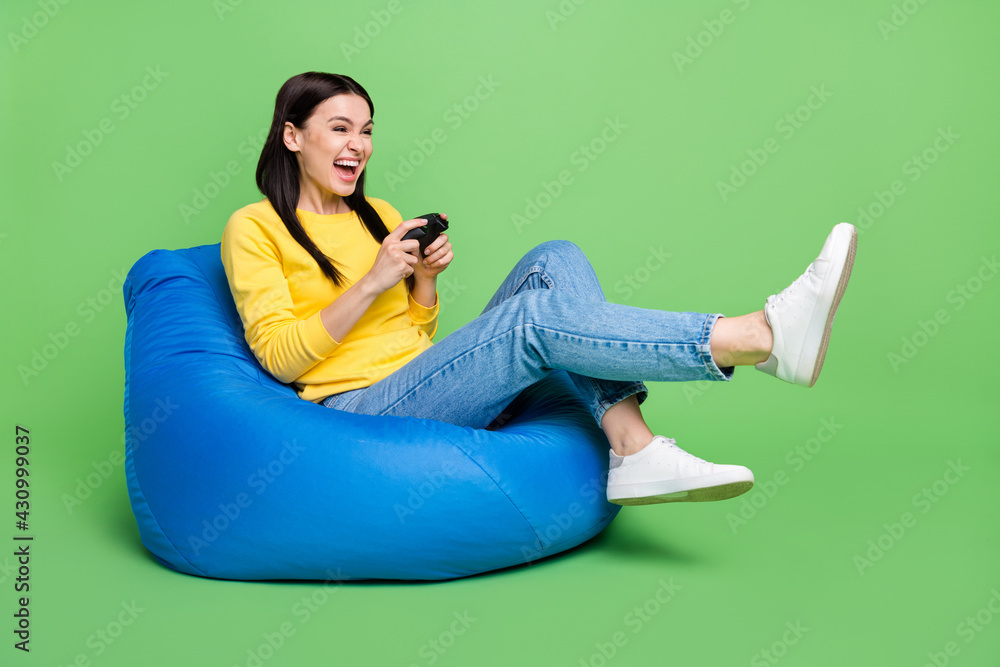Full length body size photo of woman sitting beanbag laughing playing video game isolated vibrant green color background Full length body size photo of woman sitting beanbag laughing playing video game isolated vibrant green color background