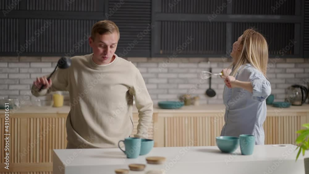 Funny couple rear view dancing while cooking together in kitchen, young active family having fun laughing feels carefree happy enjoy preparation food breakfast or dinner lifestyle leisure mood concept