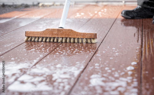 Detail of a scrubbing brush during spring cleaning on a wooden terrace with soap and splashes of water