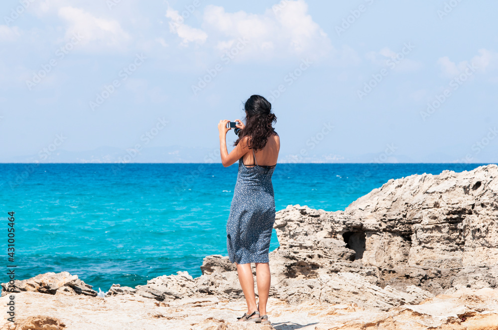 Young traveler takes pictures with her smartphone of the horizon over the sea enjoying her summer trip to the island of Formentera, a true vacation paradise in Spain