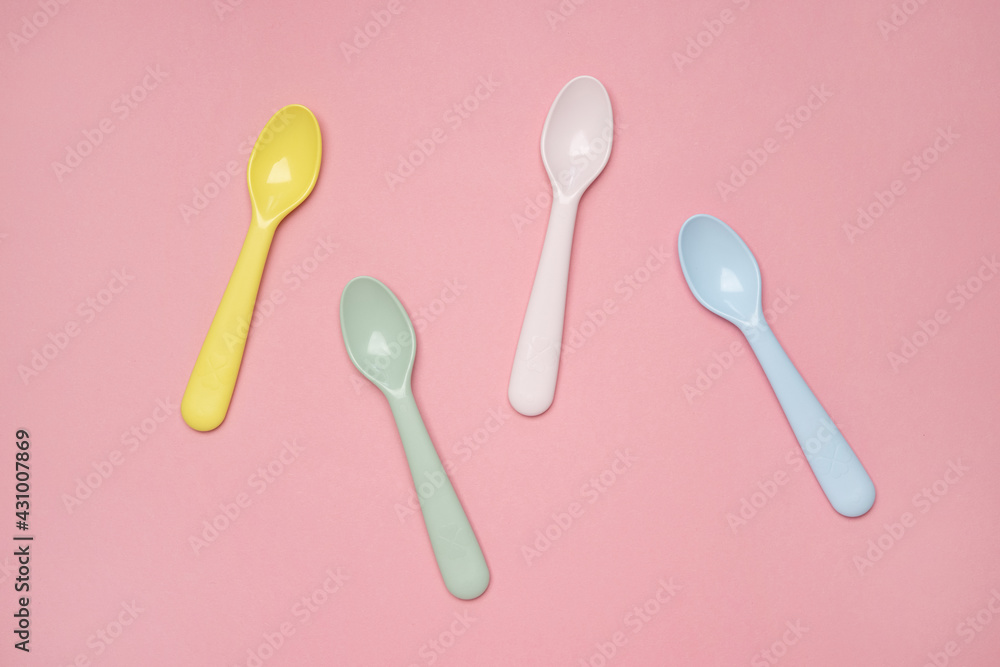 Kid spoons in different colors laid on sweet pink pastel background, a set of colorful spoons, pastel palette spoons Kid spoons in different colors laid on sweet pink pastel background, a set of colorful spoons, pastel palette spoons