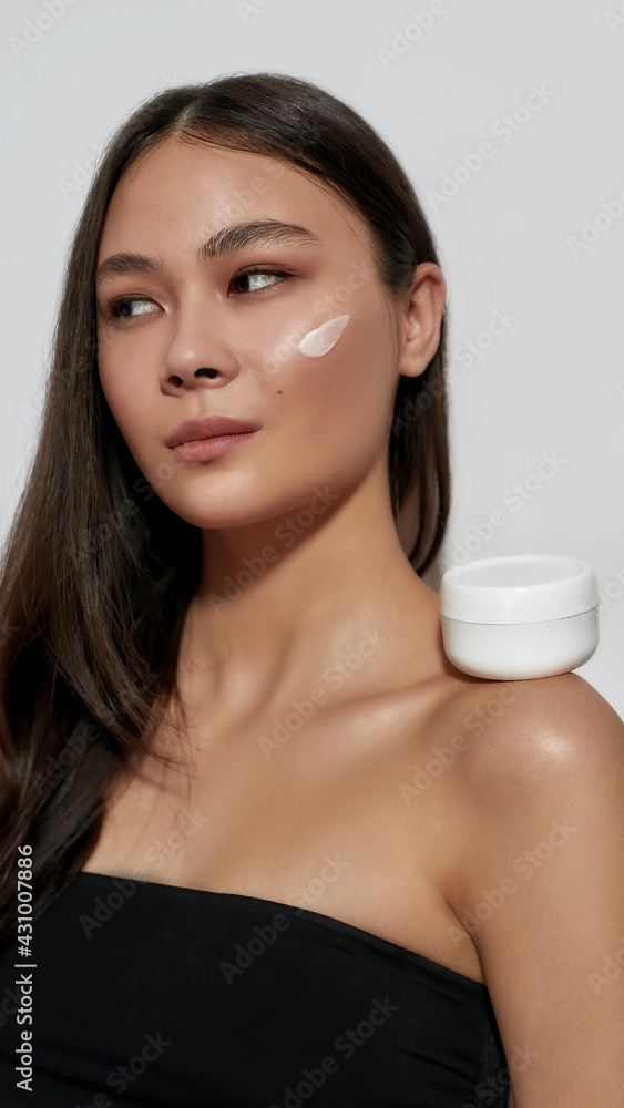 Young asian woman with facial cream smear on cheek Young asian woman with facial cream smear on cheek