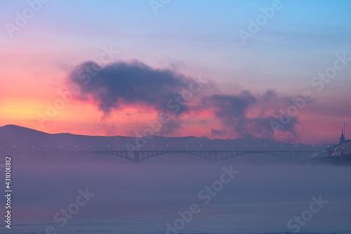 Bridge and fog across the river on the background of a beautiful sunset in winter