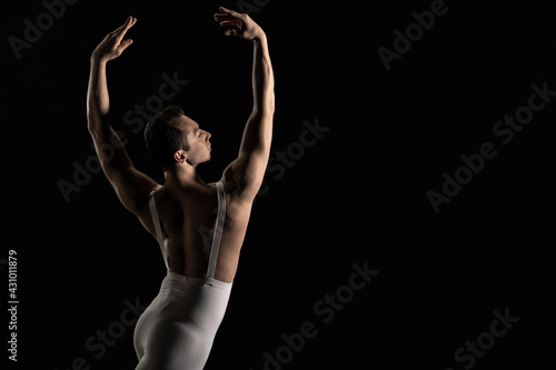 Male ballet dancer performs ballet dance element on a black background
