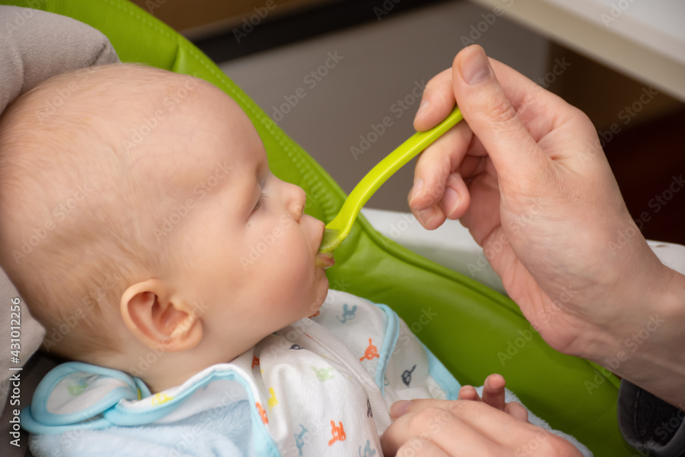 Adult feeding little baby boy with first solid food. Giving a spoon with baby puree. Adult feeding little baby boy with first solid food. Giving a spoon with baby puree.