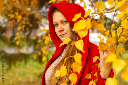 Young beautiful sexy girl in a red coat in the autumn forest among the yellow foliage