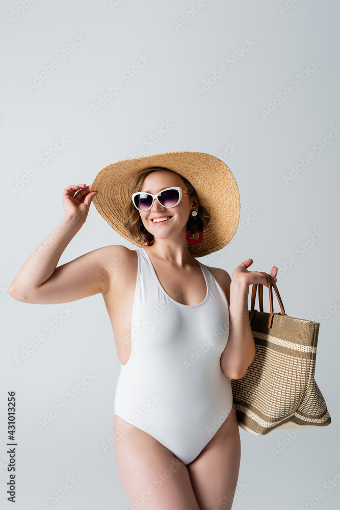 overweight and joyful woman in sunglasses and swimsuit holding bag while adjusting straw hat isolated on white overweight and joyful woman in sunglasses and swimsuit holding bag while adjusting straw hat isolated on white