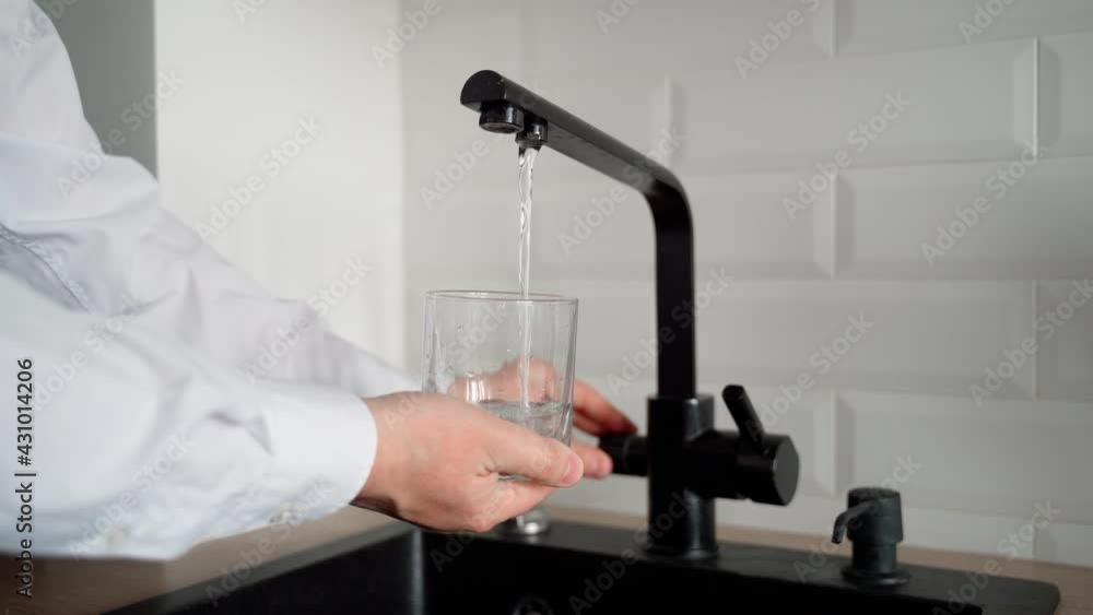 A man fills an empty glass with drinking water in the kitchen. Water