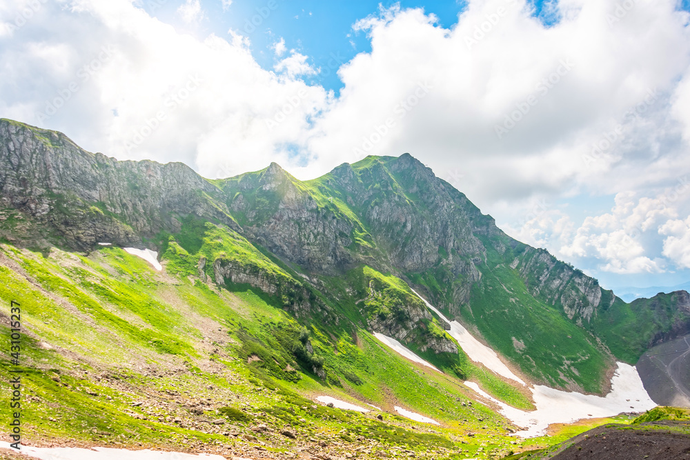 Grass meadows and ice snow in summer mountains, view of ridges and clouds.