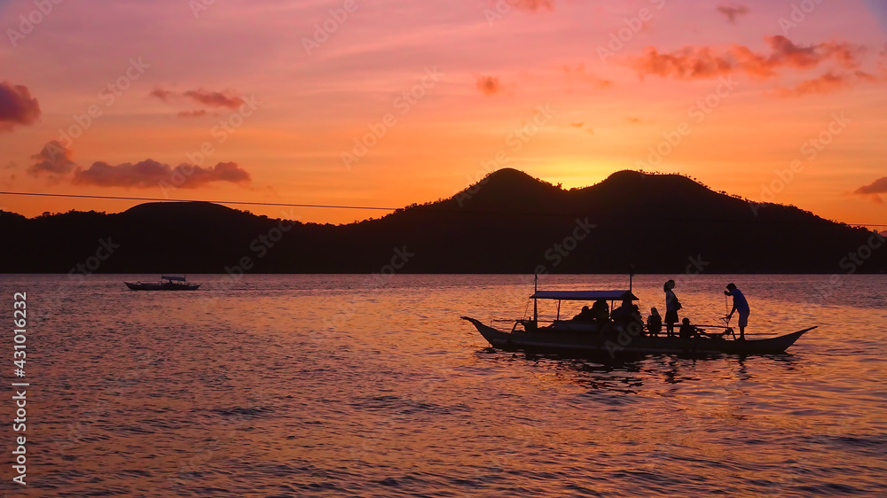 silhouette of a boat in sunset on the sea tropical island philippines thailand with pink and orange clouds