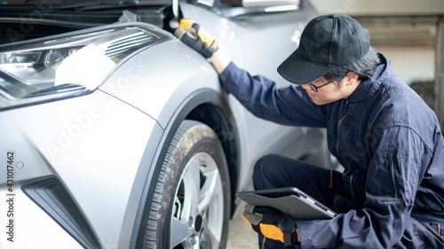 Asian auto mechanic holding digital tablet checking car wheel and tire in auto service garage. Mechanical maintenance engineer working in automotive industry. Automobile servicing and repair concept