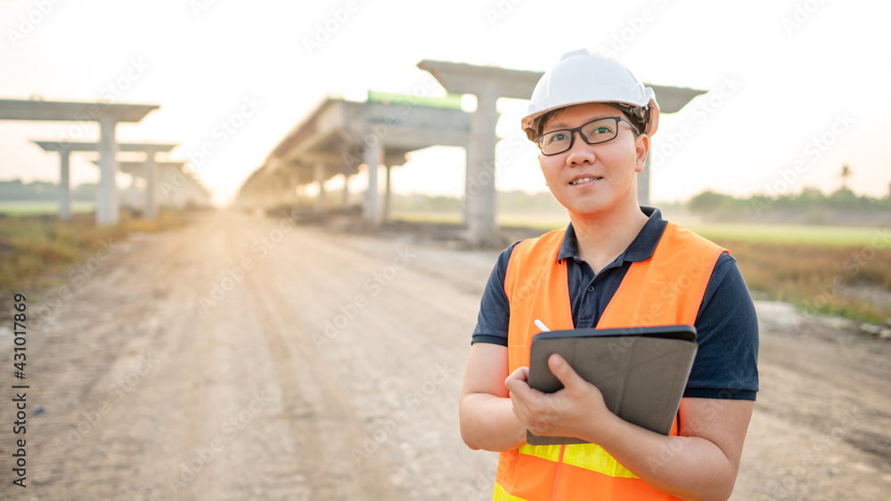 Smart Asian worker man or male civil engineer with protective safety helmet and reflective vest using digital tablet for project planning and checking architectural drawing at construction site. Smart Asian worker man or male civil engineer with protective safety helmet and reflective vest using digital tablet for project planning and checking architectural drawing at construction site.