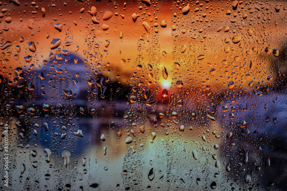 Raindrop on the window, backgorund is bluried a light of city. City life in night in rainy season abstract background.