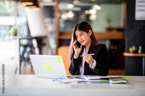 Portrait of Business young woman working on laptop computer doing finances,accounting analysis,report,data and pointing graph at the office.