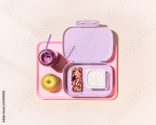 The concept of healthy school meals. Food composition with lunch box with yogurt, cereal bar, apple and oatmeal berries cocktail on a pink background with window light. Flat lay, horizontal banner