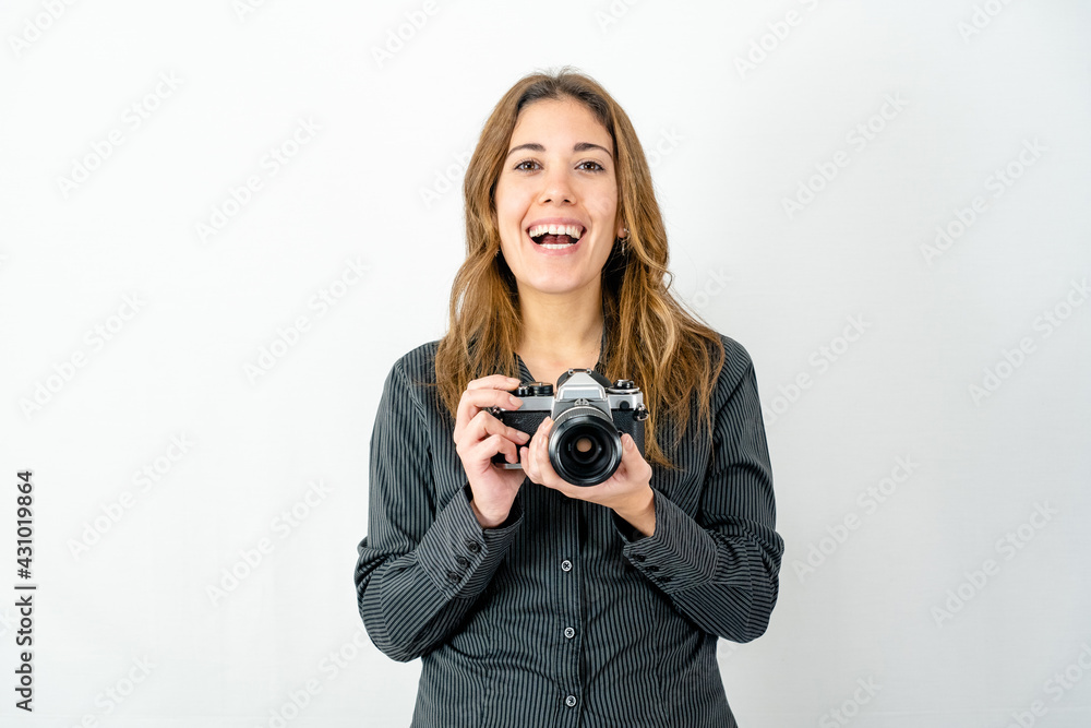 Studio shot of smiling happy young woman holding an old vintage photo camera watching photographer on white background for copy space. Concept of passion for imaging and history of classic photography Studio shot of smiling happy young woman holding an old vintage photo camera watching photographer on white background for copy space. Concept of passion for imaging and history of classic photography