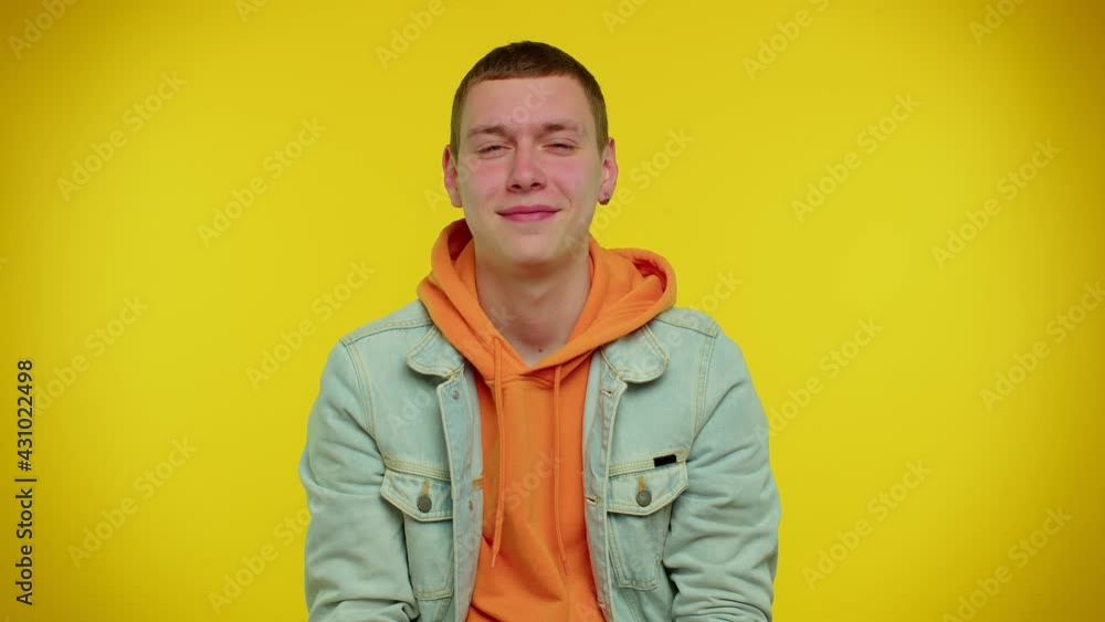 Smiling playful happy stylish teen boy in denim jacket blinking eye, looking at camera with toothy smile, winking and flirting, expressing optimism. Young handsome adult man on yellow wall background Smiling playful happy stylish teen boy in denim jacket blinking eye, looking at camera with toothy smile, winking and flirting, expressing optimism. Young handsome adult man on yellow wall background