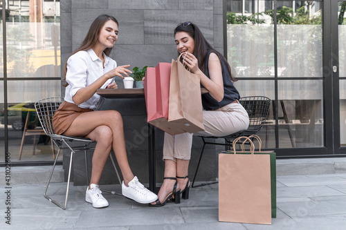 Happy and smiling young shopaholic friends women friends sit in street coffed cafe and talking after shopping and carry shopping bags in the city