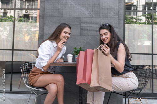 Happy and smiling young shopaholic friends women friends sit in street coffed cafe and talking after shopping and carry shopping bags in the city