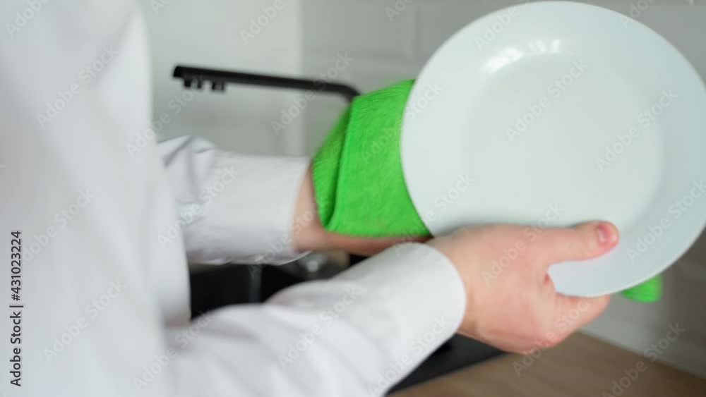 Caucasian man hands wipe wet dishes in the kitchen with a green towel. Close-up shot Caucasian man hands wipe wet dishes in the kitchen with a green towel. Close-up shot