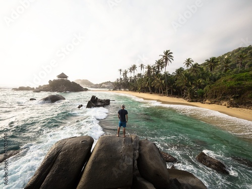 Male tourist standing on giant stone rock bolders in Tayrona National Park tropical Caribbean palm tree coast Colombia photo