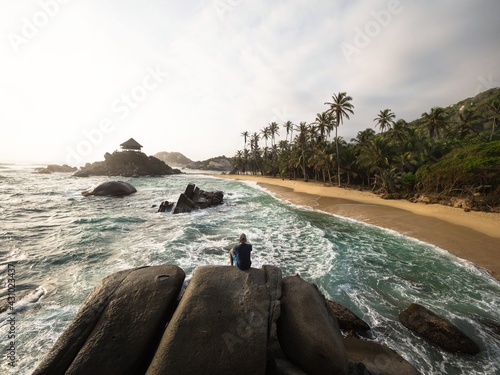 Male tourist sitting on giant stone rock bolders in Tayrona National Park tropical Caribbean palm tree coast Colombia photo